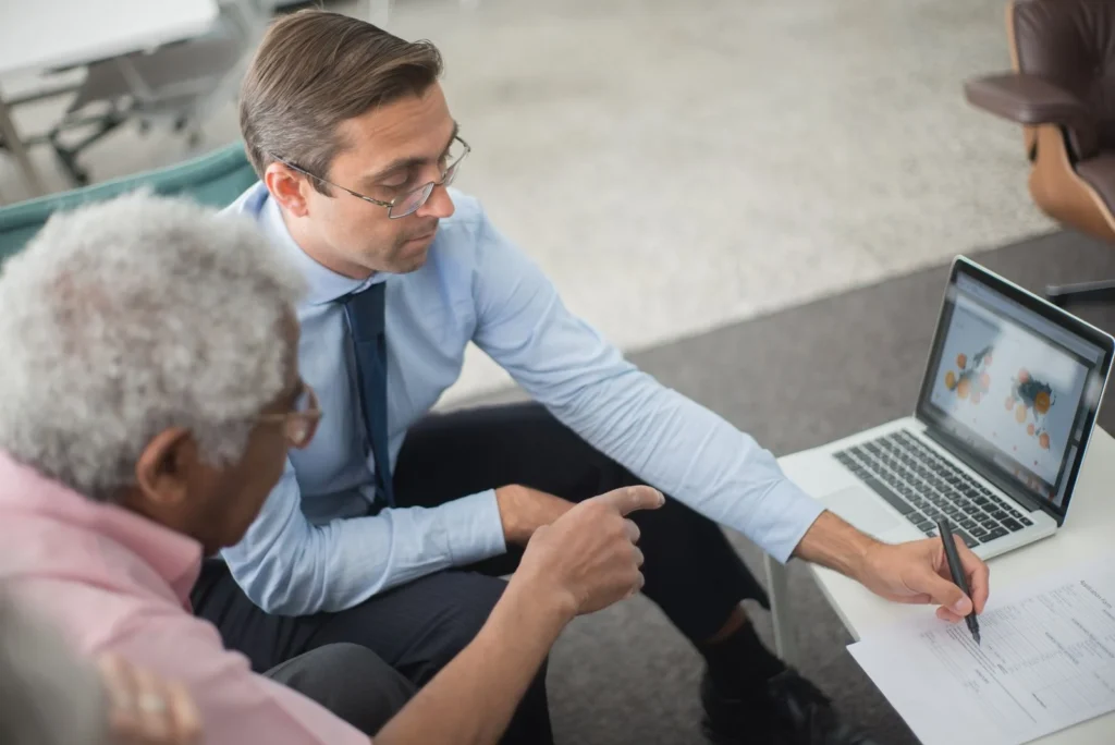 Two professionals reviewing financial documents beside a laptop