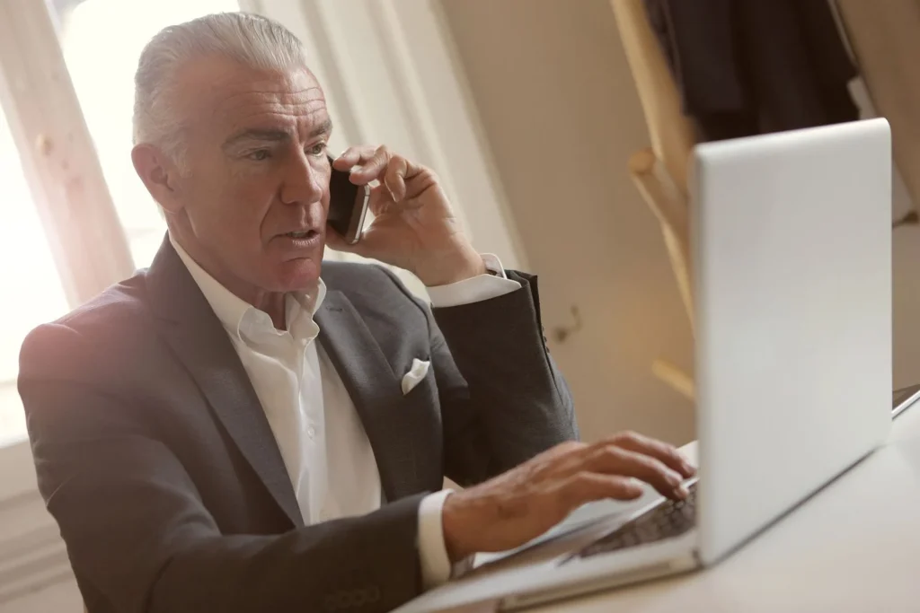 Professional checks a laptop while calling an established contact to verify a payment instruction