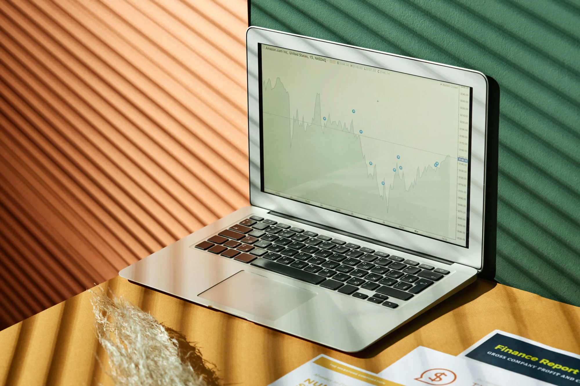 Laptop displaying a financial chart beside printed reports on a desk
