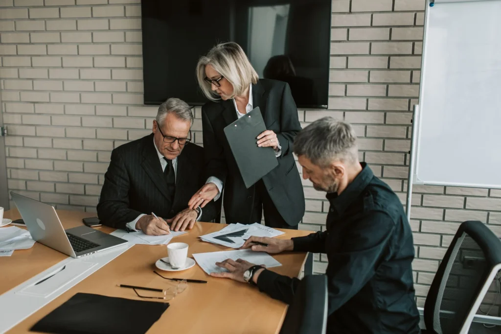 Three professionals reviewing and signing documents at a table